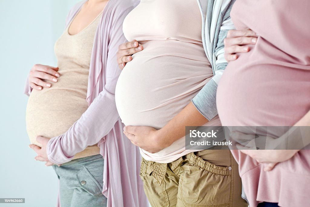 Pregnant bellies Close-up of the pregnant bellies of a three women standing in a row. Selective focus. Pregnant Stock Photo
