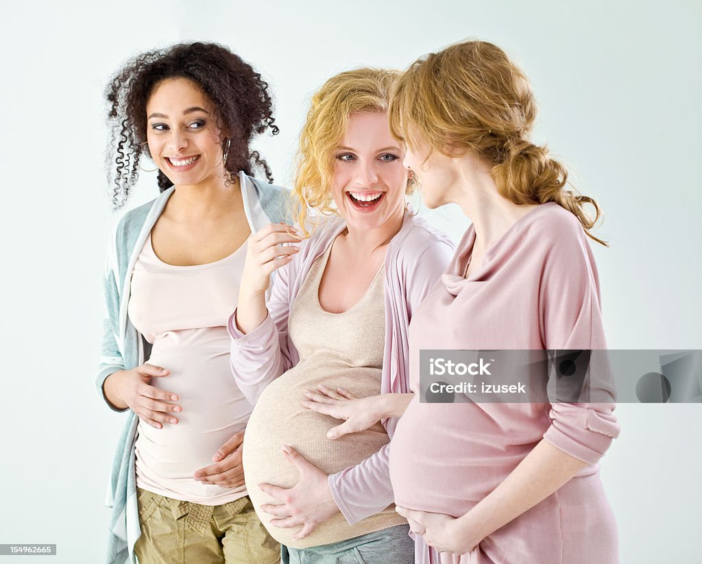 Happy pregnant women Three happy and proud, pregnant young adult women standing in a row against white background, looking at each other and smiling. Pregnant Stock Photo