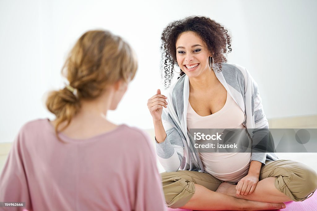 Pregnant women doing exercises Front view on preety, pregnant young adult woman sitting cross-legged on the gym mat after workout and talking with her friend. Pregnant Stock Photo