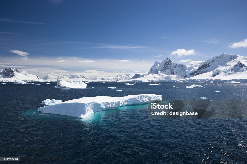 Blue sky above sea with icebergs A scenic view of Paradise Harbour in the Antarctic peninsula. Background of glaciers and snow topped mountains with still waters and an iceberg in the foreground Antarctica Stock Photo