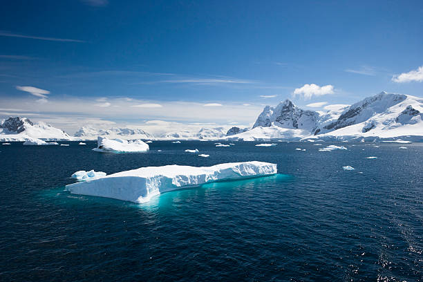 Blue sky above sea with icebergs A scenic view of Paradise Harbour in the Antarctic peninsula. Background of glaciers and snow topped mountains with still waters and an iceberg in the foreground paradise bay antarctica stock pictures, royalty-free photos & images