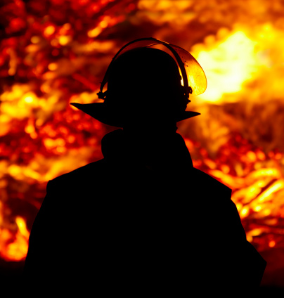 silouette of a firefighter against large fire in the dark, soft fokus