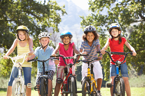 Group Of Children Riding Bikes In Countryside Wearing Cycle Helmets