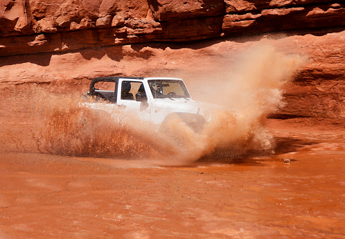 A four wheel drive off-road vehicle splashing through a large mud hole in Southern Utah.