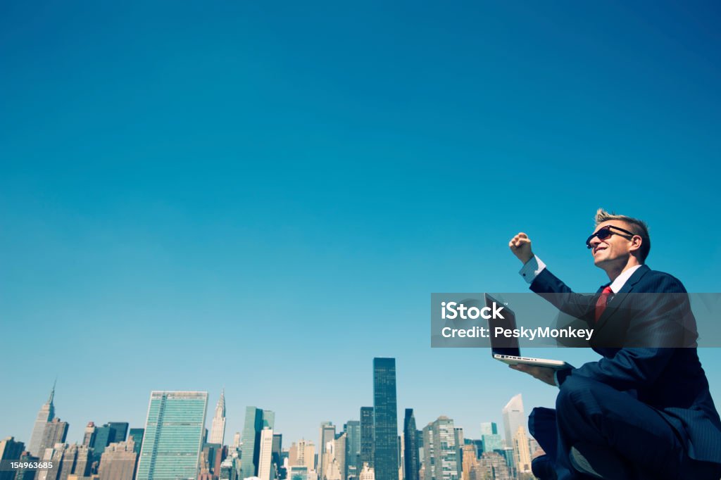 Uomo d'affari di successo pompe pugno di lavorare all'aperto sul portatile skyline della città - Foto stock royalty-free di Computer portatile
