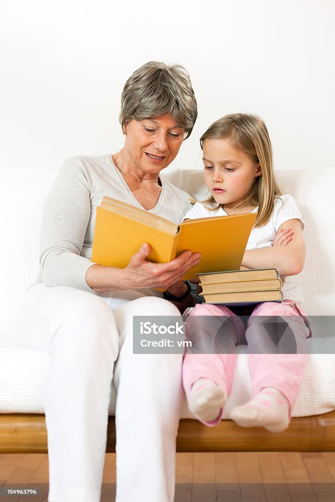 Senior Woman Reading To Little Girl Grandmother and her granddaughter are reading a storybook on the couch. 6-7 Years Stock Photo