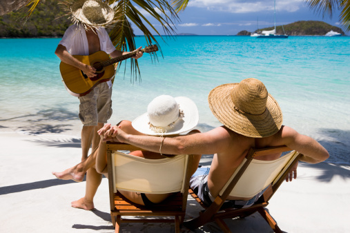 honeymoon couple relaxing at a beach in the Caribbean and listening a local musician playing serenade on a guitar