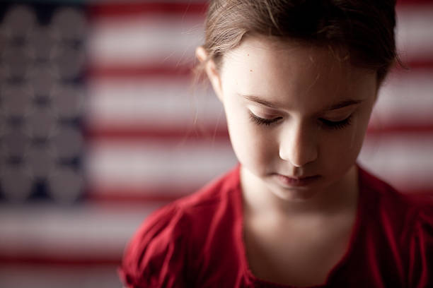 jeune fille triste regardant vers le bas devant le drapeau américain - child grief mourner disappointment photos et images de collection