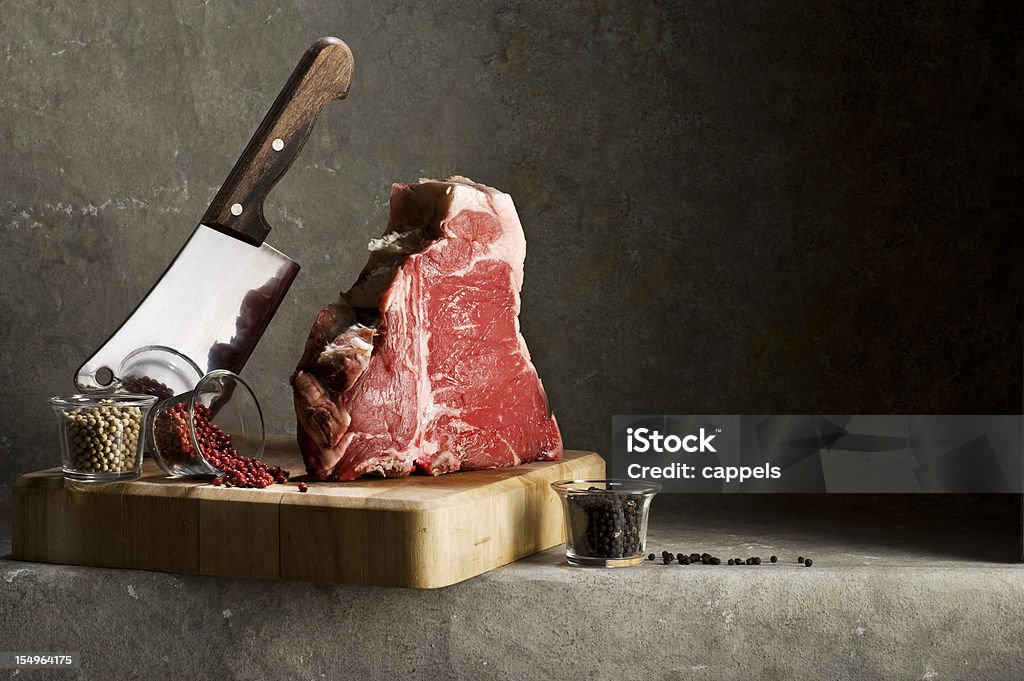 Florentine T-Bone Steak.Color Image A very thick,juicy and tender steak,called Florentine t-bone steak,shot  on a chopping board with a cleaver and different kind of pepper,white,red and black. Meat Stock Photo