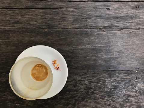 finished cup of hot cappuccino coffee with decorated pretty small flowers on its white saucer on a natural dark brown wood table