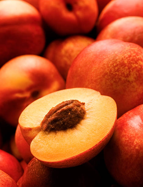 A yellow peach opened on top of other peaches juicy peach open, leaning on other colorful peaches. nectarine stock pictures, royalty-free photos & images
