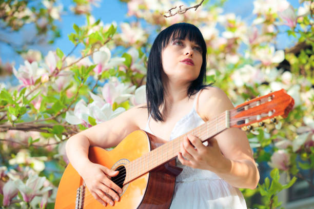 young woman sitting in a magnolia tree and palying a tune on her guitar