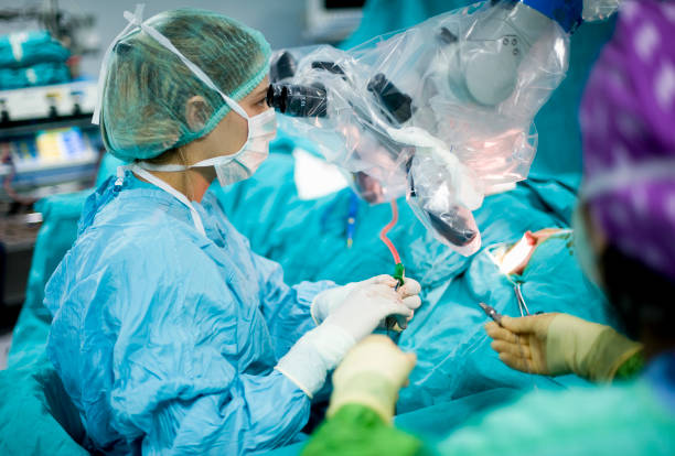 a female surgeon using a surgical microscope during surgery - robotchirurgie stockfoto's en -beelden