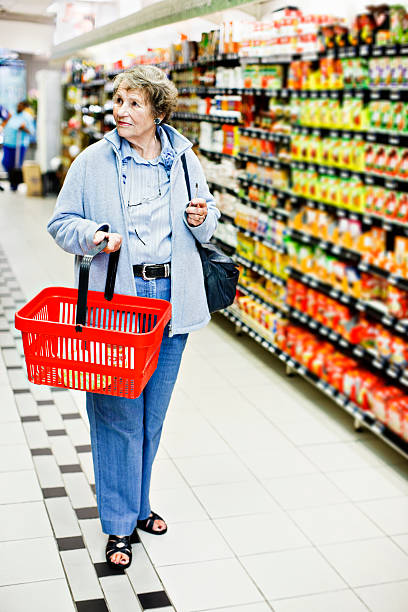 senior donna shopper con cestino di plastica look in supermercato - senior adult aging process supermarket shopping foto e immagini stock
