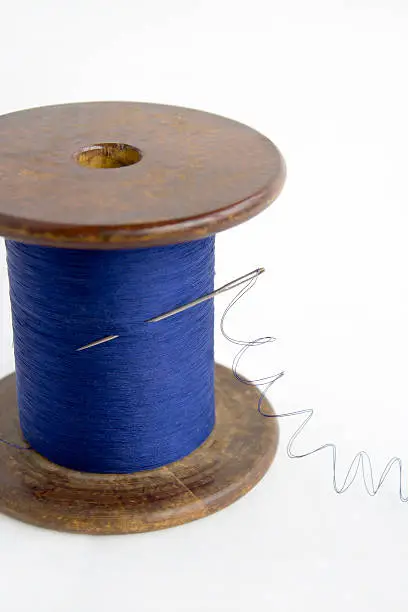 Spool of blue thread with a needle on a white background