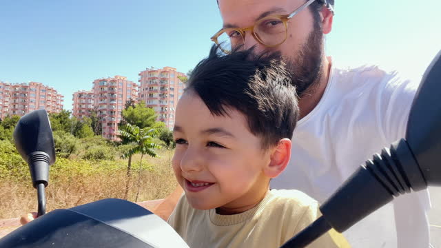 Video Footage of a young father and son riding a moped scooter on a bright sunny day