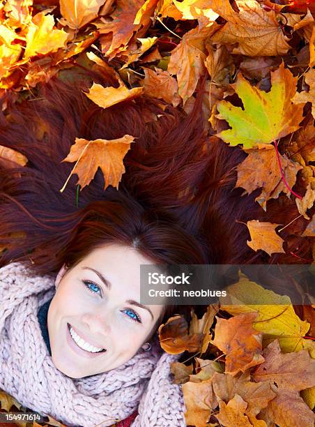 Foto de Mulher Com Cabelo Vermelho Coloca Sobre Folhas De Outono e mais fotos de stock de 20-24 Anos