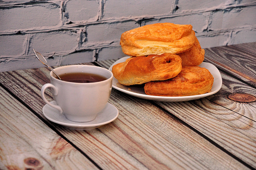 A cup of hot tea and a plate with several puff pastries on a wooden table. Close-up.