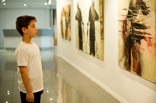 Minimal portrait of teenage boy looking at abstract art on wall in art gallery or museum, copy space