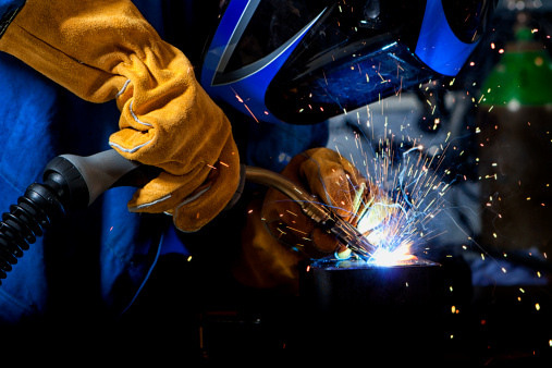 Welder wearing gloves and mask with welding sparks.