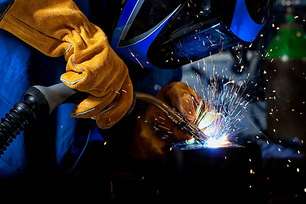 Welder wearing gloves and mask with welding sparks.