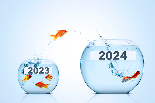 Golden fish leaping from a smaller aquarium to a larger aquarium with 2024 new year numbers over blue background