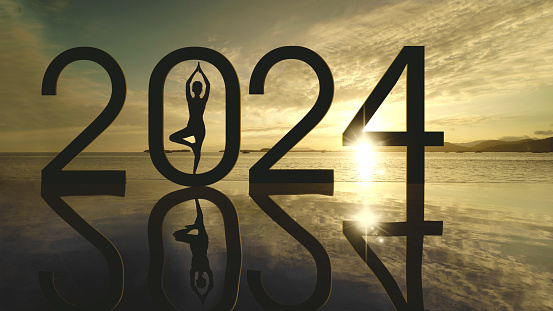 Silhouette of young woman exercising yoga while doing meditation with 2024 new year numbers on the beach at sunrise time