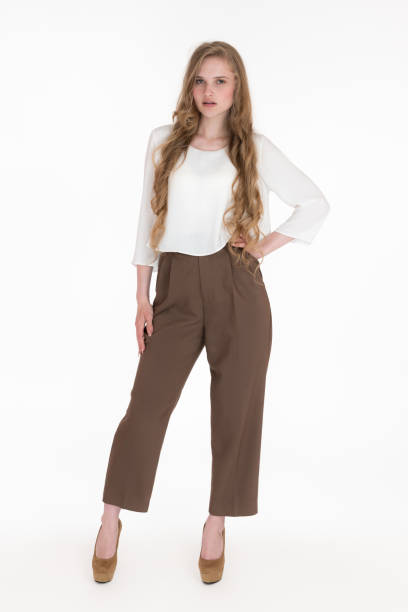 Young blonde female with long hair wearing white blouse, brown pants, shoes standing in full length stock photo