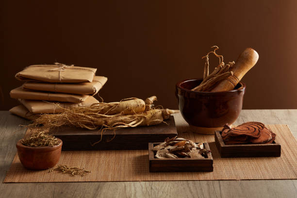 TRADITIONAL MEDICINE Advertising scene for product with herbal ingredient. Ginseng and healthy herbs are placed on wooden trays, decorated with pestles, mortars and paper-wrapped prescriptions on a brown background. codonopsis pilosula stock pictures, royalty-free photos & images