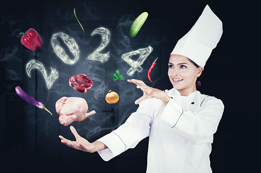 Indian female magician chef with flying food ingredients and smoke shaped of 2024 new year numbers in the kitchen