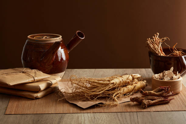 TRADITIONAL MEDICINE Porcelain pot with ginseng and rare herbs displayed on wooden table top and brown background. Medicines originating from ancient China, health-protecting foods. Front view, copy space codonopsis pilosula stock pictures, royalty-free photos & images