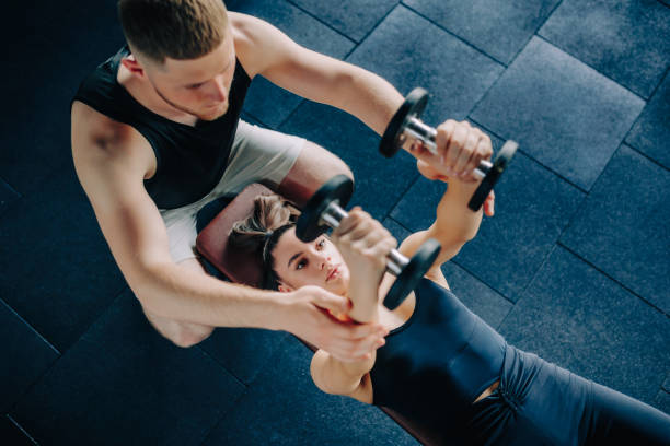 istock Dumbbell Exercise Male Personal Trainer Supports Woman's Workout 1549838050