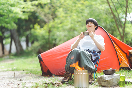 Young Japanese woman is doing solo camping and drinking.