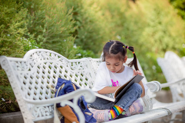 istock Back to school. Asian girl reading a book. Primary school students after classes learning homework. 1549867758