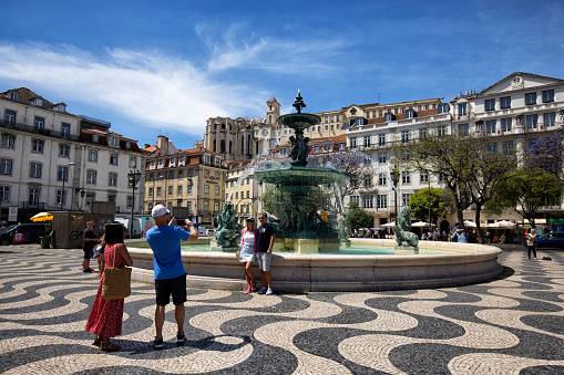 Lisbon, Portugal - Street view of Baixa district on a summer afternoon. People and a fountain can be seen in the Rossio Square.