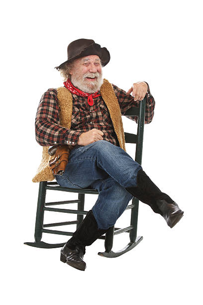 Laughing old cowboy sits in rocking chair Classic old west style laughing cowboy with felt hat, grey whiskers, revolver. He sits legs crossed in a rocking chair. Isolated on white, vertical, copy space. checkered cowboy boots stock pictures, royalty-free photos & images