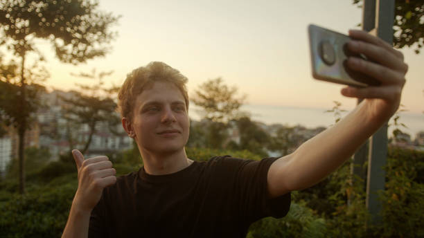 istock Capturing Moments: Handsome Blond Young Man Taking Selfies with His Smartphone, Striking Various Poses Outdoors 1549985666