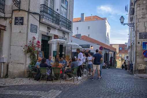 Lisbon, Portugal - Street view of Alfama district on a summer afternoon. A sidewalk restaurant with many people.