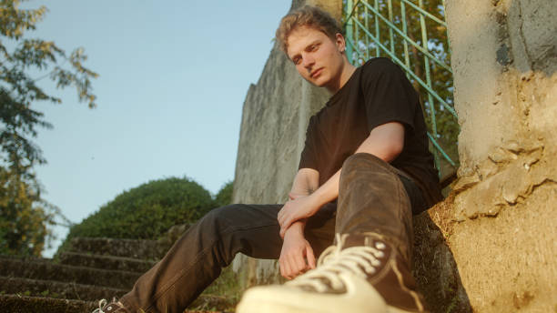 istock Handsome Young Blond Male Model Sitting by the Wall, Striking a Pose and Gazing 1549987775