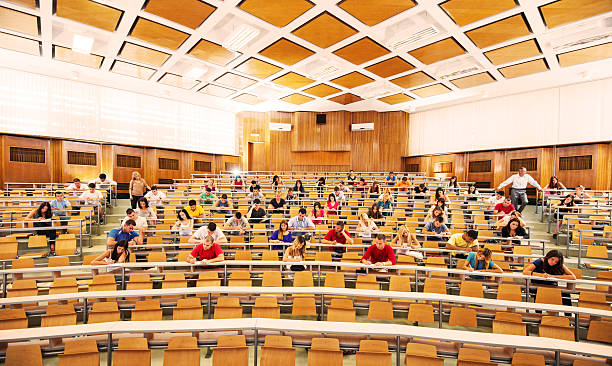 Group of college students in the university amphitheatre, they are sitting and doing an exam. Two professors are monitoring the students.   