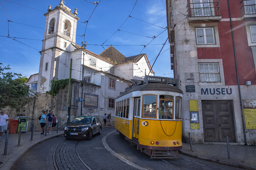 Lisbon, Portugal - Street view of Alfama district on a summer afternoon. A yellow Tram and people past Igreja de Santa Luzia church.