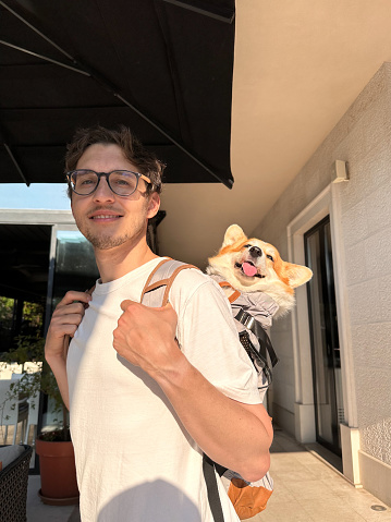 Young man carrying his cute corgi in a backpack. Travelling with dog