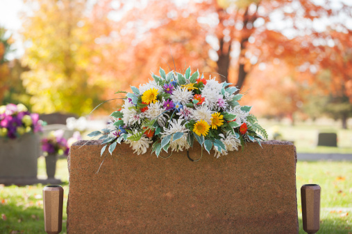 A colorful spray of flowers grace the top of a tombstone in the fall.