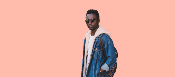 istock Stylish young african man model wearing denim jacket, backpack isolated on pink background, blank copy space 1550020390