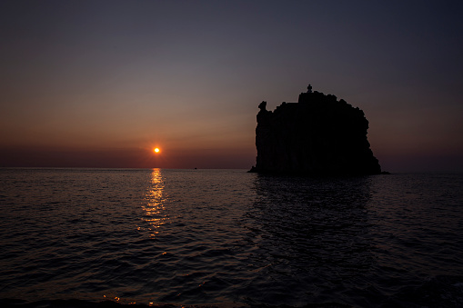 The last rays of sunshine illuminating the calm waters around Strombolicchio Island