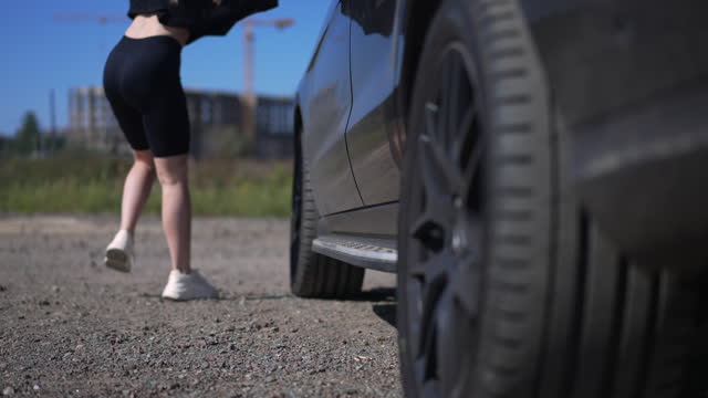 Female legs walking out car and unrecognizable young woman leaving in slow motion. Confident Caucasian female driver and vehicle in sunshine outdoors.