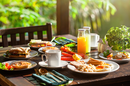 Delightful breakfast served by serene lake in Thai resort. Savor delicious meal featuring assortment of dishes like sandwiches, salads, and freshly squeezed orange juice. Concept: Thailand vacation.