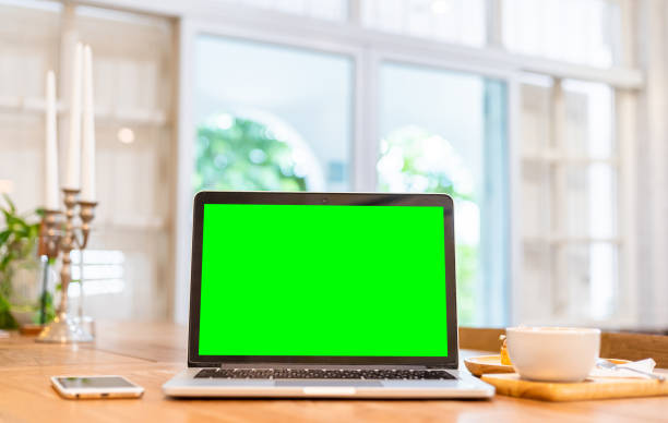 istock Mockup of laptop computer with empty screen with coffee cup and smartphone on table of the coffee shop background,Green screen 1550112348