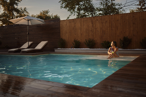 Carefree woman enjoying in the sunlight while relaxing with a drink in the pool at the backyard.