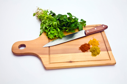 Wooden board with chopped garlic, a whole clove of garlic, parsley and a knife on a white background, top view. Cooking homemade vegetable stew or other dish
